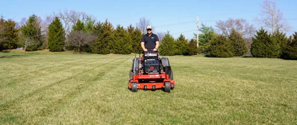 Worker riding a red mower on a lawn in Mission, KS.